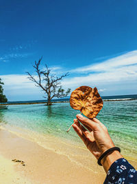 Man holding umbrella by sea against sky