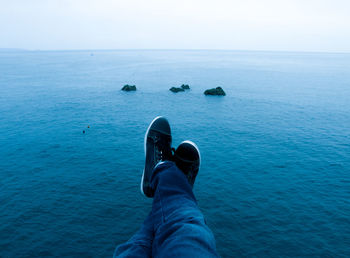 Low section of man sitting over blue sea against sky
