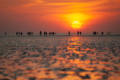 Silhouette people on beach against orange sky