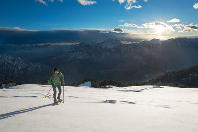 Rear view of man walking on snow covered mountains against sky during sunset