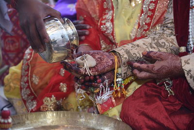 Cropped image of person pouring water on bride and bridegroom hands during wedding ceremony