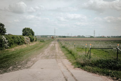 Road passing through field against cloudy sky