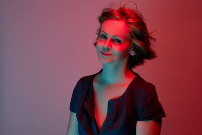 Portrait of smiling woman with hand in hair against red background