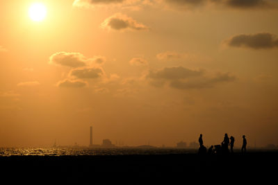 Silhouette people on land against sky during sunset
