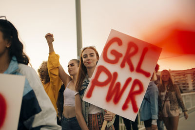 Portrait of women protesting with friends for human rights in city against sky