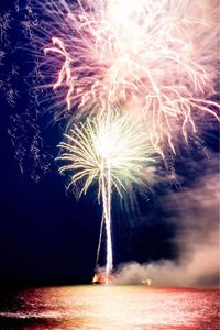 Low angle view of fireworks in sea against sky at night