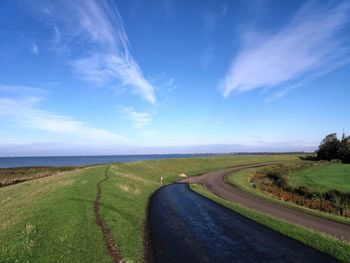 Empty road amidst field against sky