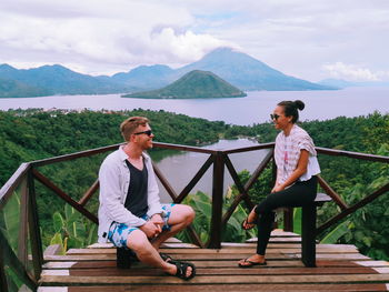 Woman sitting on railing against mountains and sky