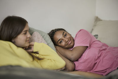 Smiling female teenager relaxing on bed with friend in bedroom at home