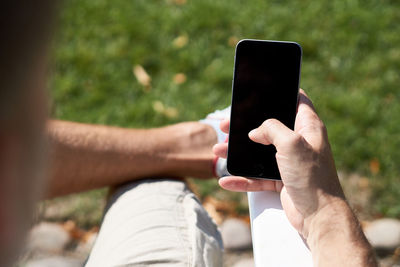 Cropped image of man using blank phone while sitting outdoors