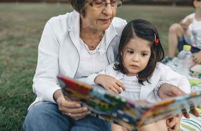 Grandmother showing picture book to granddaughter on meadow