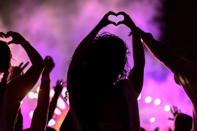 Rear view of people making heart shapes during music concert at night