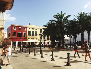 People by palm trees in city against sky