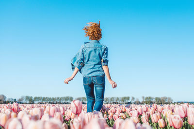 Rear view of woman standing on field against clear blue sky