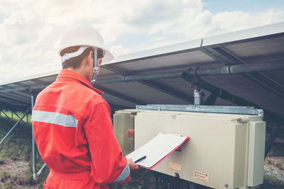 Side view of worker talking on phone while standing by solar panel