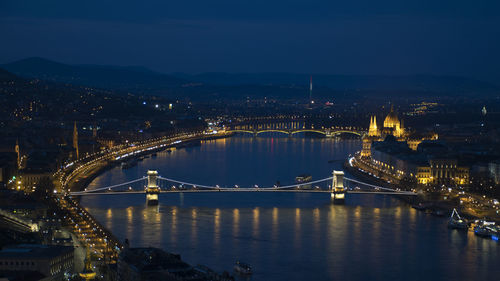 Illuminated bridge over river in city at night