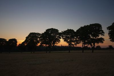 Silhouette trees on field against clear sky