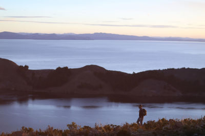 Man on field by sea against sky during sunset