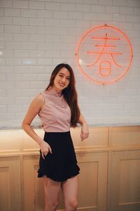 Portrait of smiling young woman standing against wall