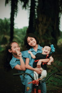 Portrait of happy sisters with bicycle at park