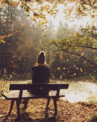 Rear view of woman sitting on bench during autumn