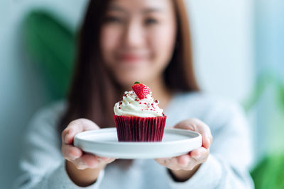 A beautiful asian woman holding and showing a plate of red velvet cupcake