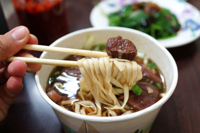 Cropped hand eating noodles on table