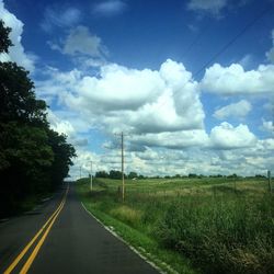 Road passing through field against cloudy sky