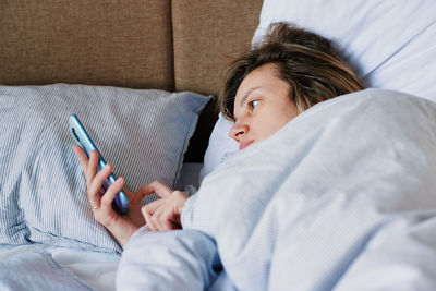 Woman using smartphone in the bed, social media, lazy weekend