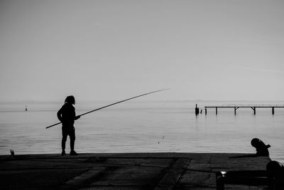 Man fishing on pier over sea against sky