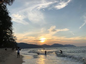 Silhouette people on beach against sky during sunset