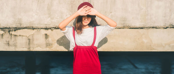 Young woman shielding eyes while standing against wall