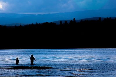 Silhouette people on lake against sky