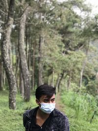 Young man wearing mask looking away while standing in forest