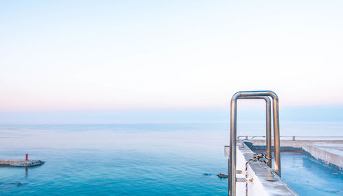 Ladder on a rooftop by sea against sky