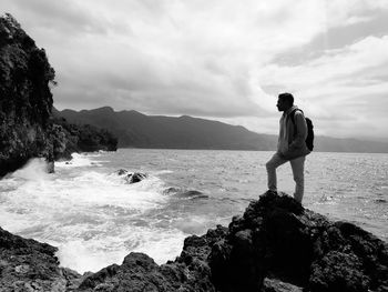 Man standing on rock by sea against sky