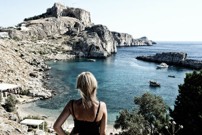 Rear view of woman standing on cliff by sea against clear sky