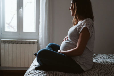 Midsection of woman sitting by window at home