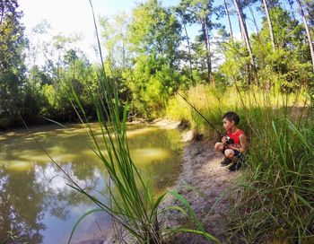 Boy fishing in river while crouching at riverbank