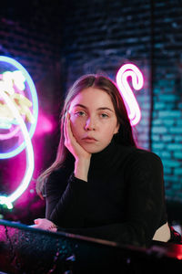 Close-up portrait of beautiful young woman sitting against illuminated lights