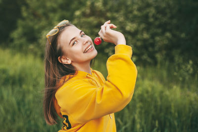A smiling girl in a bright yellow sweater holds a bright red lollipop. summer nature, lifestyle