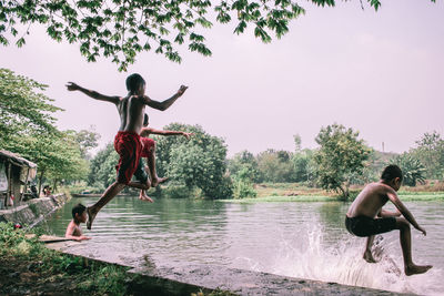 Full length of shirtless man jumping in swimming pool against sky