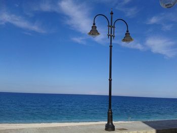 Street light by sea against blue sky