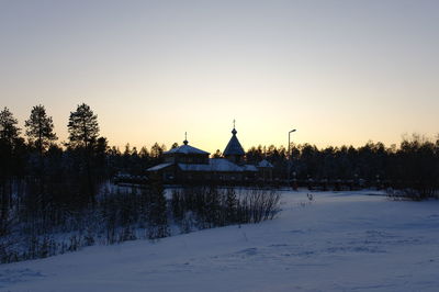 Built structure on snow covered field against sky during sunset