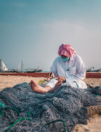 Man working with fishing net on beach against sky