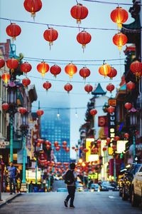 Full length rear view of man walking in city street above chinese lanterns at dusk