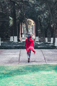 Full length rear view of man with red carpet and top hat walking towards ancient gate