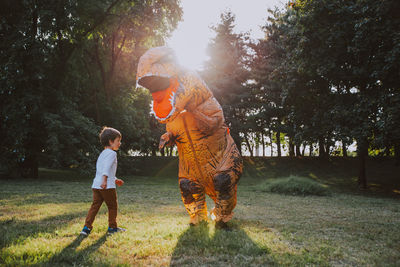 Boy playing with person wearing dinosaur costume in park