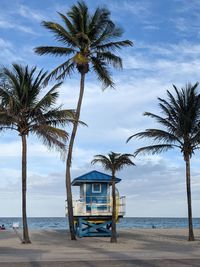 Lifeguard shack with palm trees on beach against sky