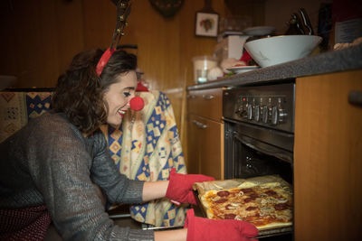 Side view of smiling woman baking food in oven at home